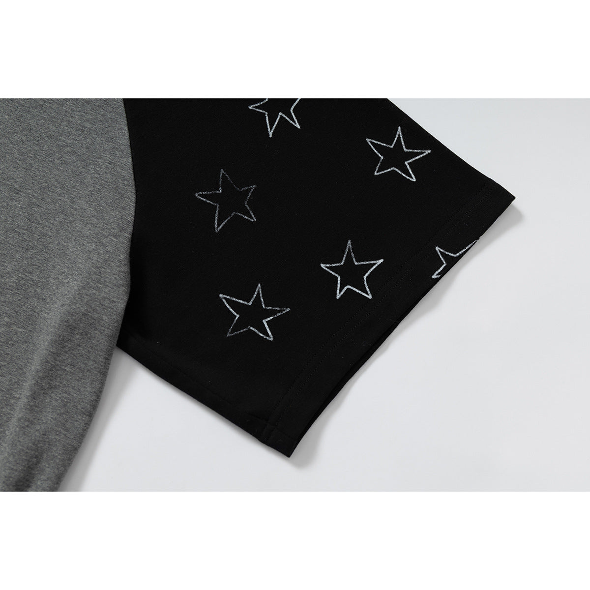 Close-up of the black T-shirt sleeve, patterned with outlined white stars, beside the gray body.