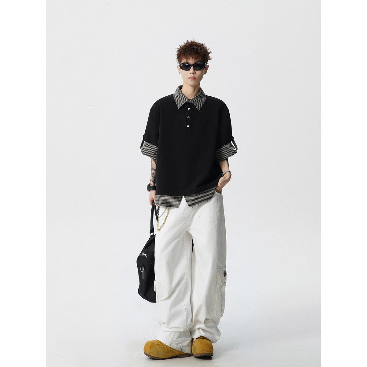 Full-length model wearing a black polo with checked collar, cuffs and hem, loose white trousers and tan shoes.