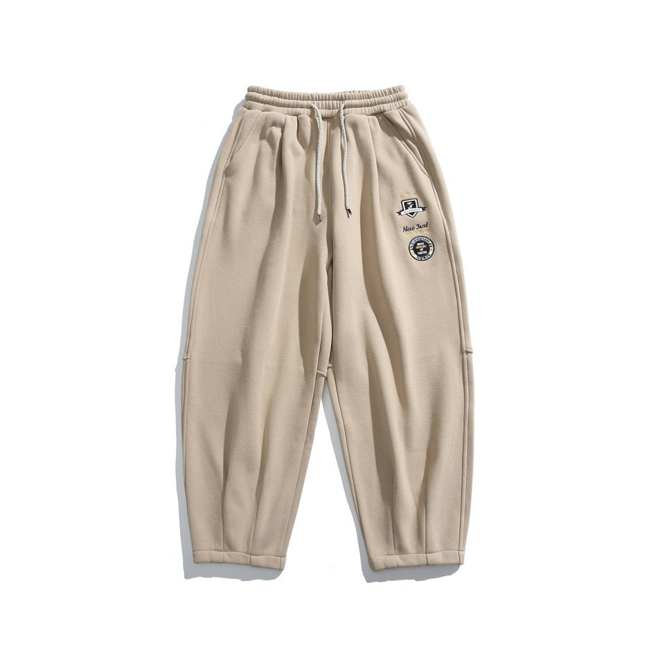 Khaki sweatpants flat lay with drawstring waist, side pockets and embroidered badges on the left leg