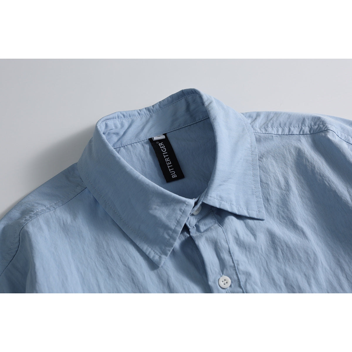 Close-up of a light blue shirt collar, placket, and white button, with a black neck label.