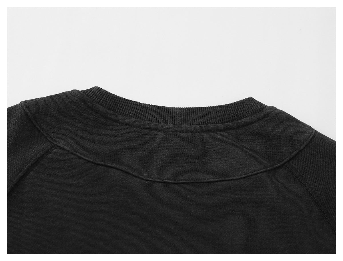 Close-up of a black garment’s ribbed crew neckline and curved shoulder seams.