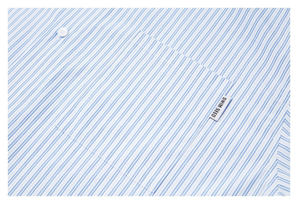 Close-up of a white garment with fine blue stripes, a white button, pocket seam, and small sewn label.