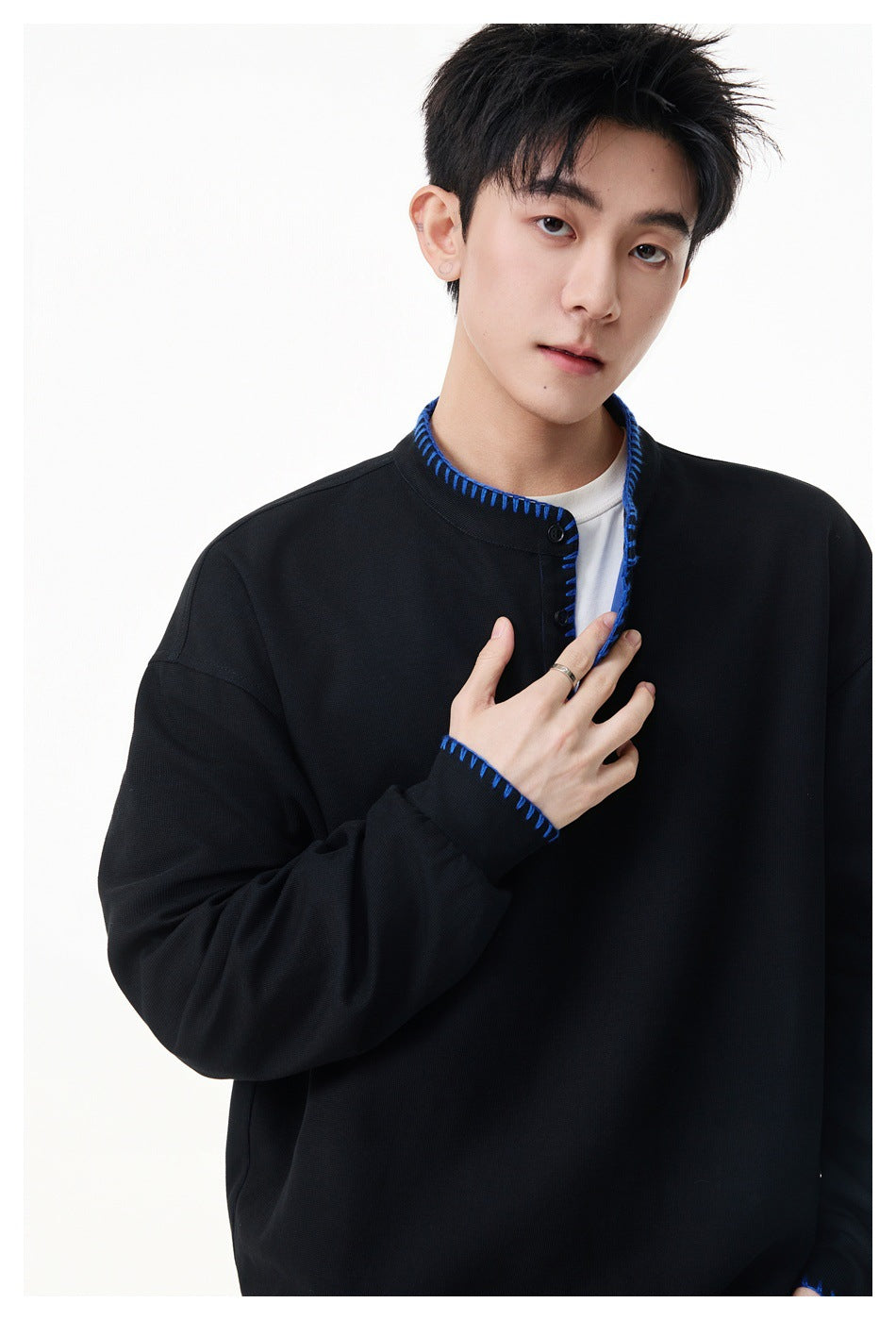 Close view of a model wearing a black pullover, highlighting blue stitching around the collar, placket and cuff.