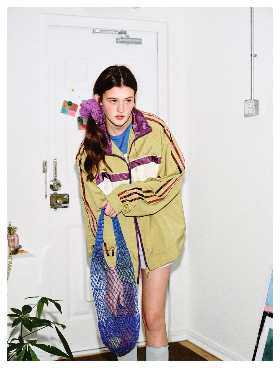 Model wearing an olive track jacket with purple and cream chest panels and burgundy sleeve stripes.