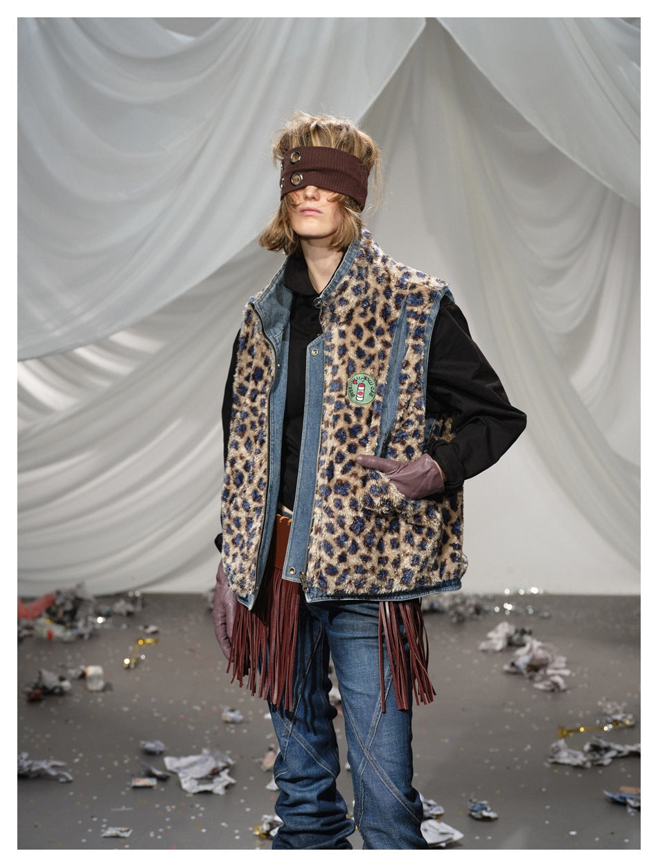 Model wearing a blue denim-trimmed vest with a tan and navy leopard pattern, layered over a black top and jeans.
