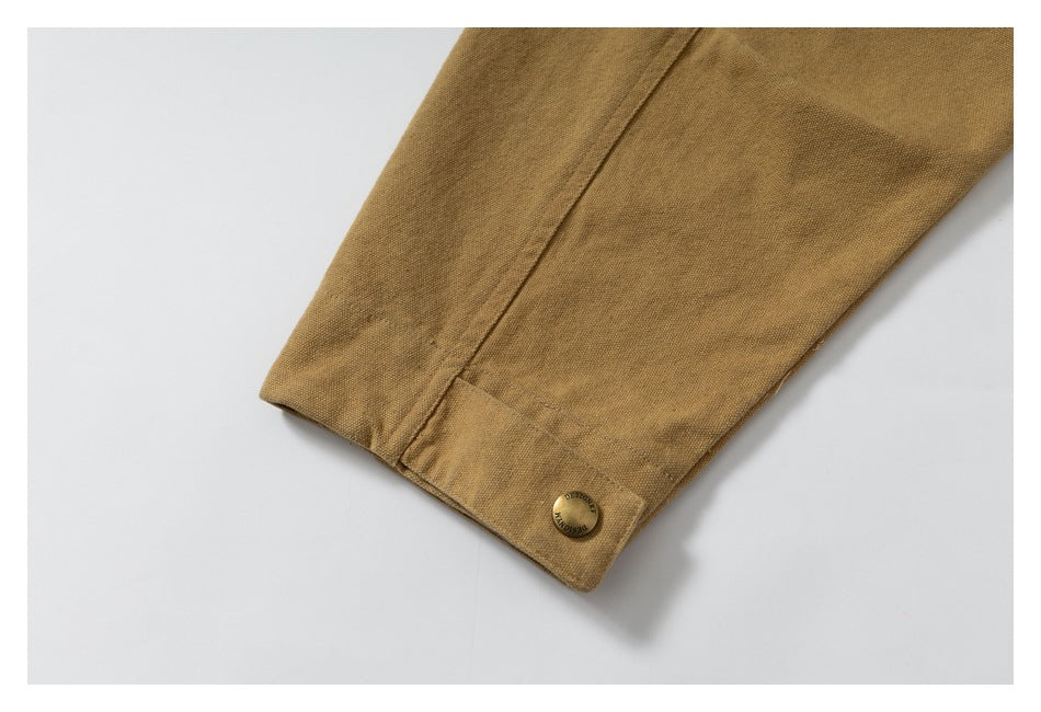 Close-up of the mustard-brown jacket cuff with a stitched seam and round metal snap button.