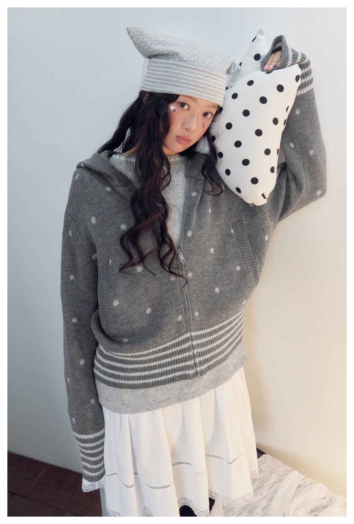 Closer view of a model in a gray hooded cardigan with white motifs and striped hem, over a white dress.