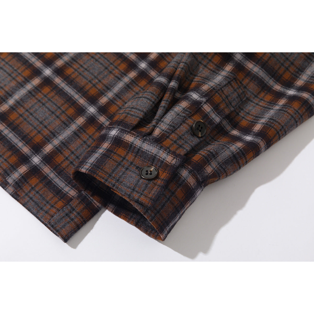 Close-up of a gray, rust, and black plaid shirt cuff with two dark buttons.