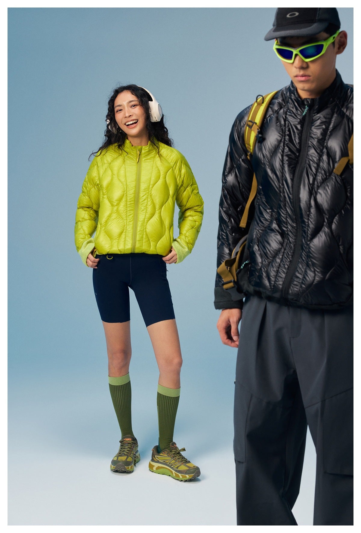 A woman models a lime quilted zip jacket while a man in a black jacket is partly cropped in the foreground.