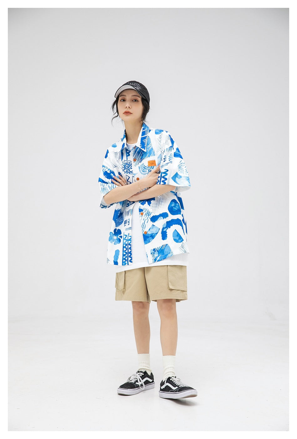 Model wearing blue and white abstract print short-sleeve shirt open over a white tee with khaki shorts