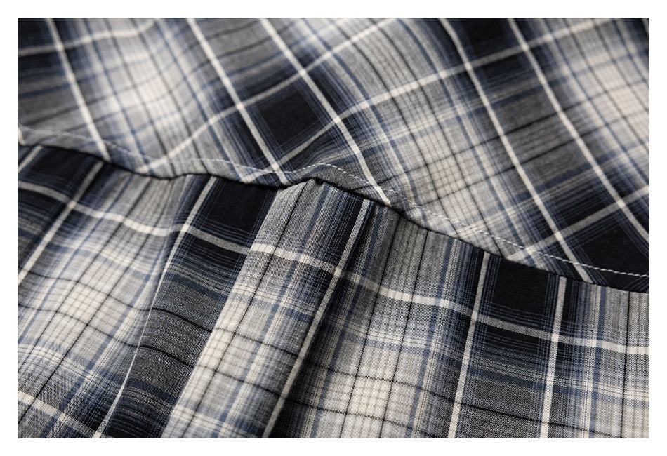 Close-up of a stitched seam across black, gray, and cream plaid shirt fabric.