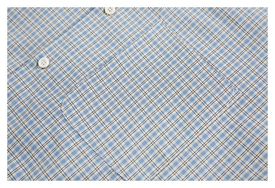 Close-up of the rounded chest pocket and white buttons on a blue plaid shirt.