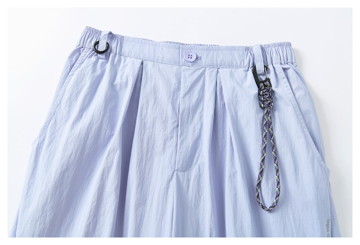 Close-up of pale lavender pants showing the front waistband, button, pleats, and a decorative cord loop.