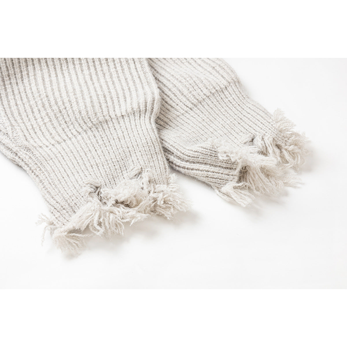 Close-up of two ivory rib-knit sweater cuffs with heavily frayed edges.