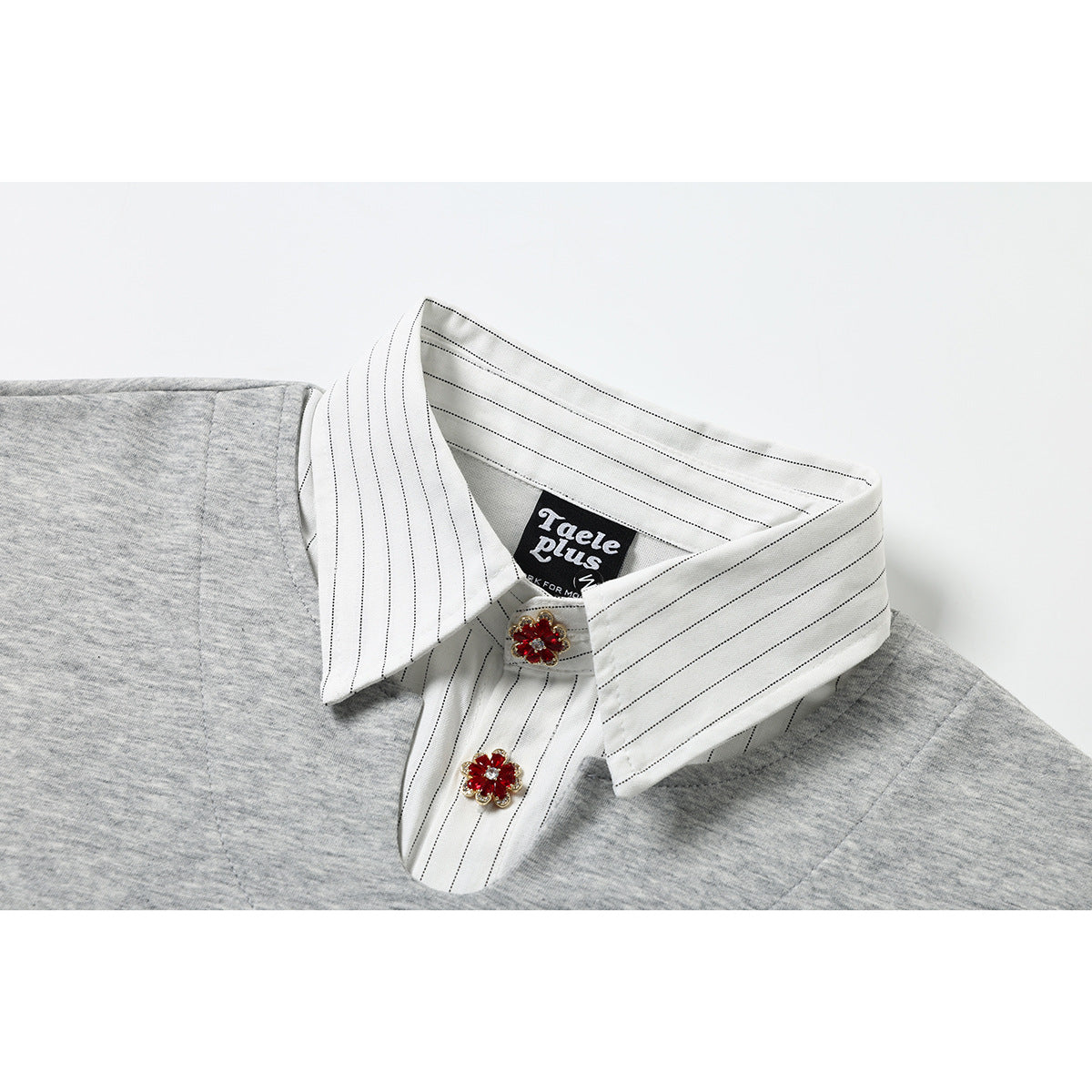 Close-up of a gray shirt's white pinstriped collar and placket, with two red jeweled flower buttons.