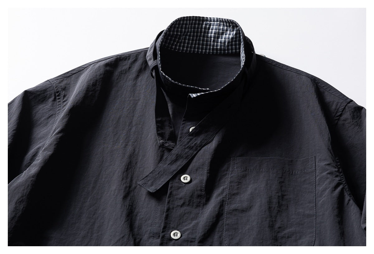 Close front view of a dark charcoal shirt with an open stand collar, checked inner collar, chest pocket, and pale buttons.