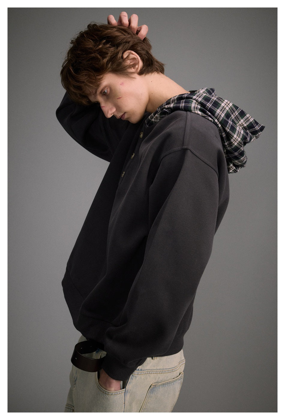 Side view of a model wearing a charcoal hoodie with a black-and-white plaid hood lining and button placket.