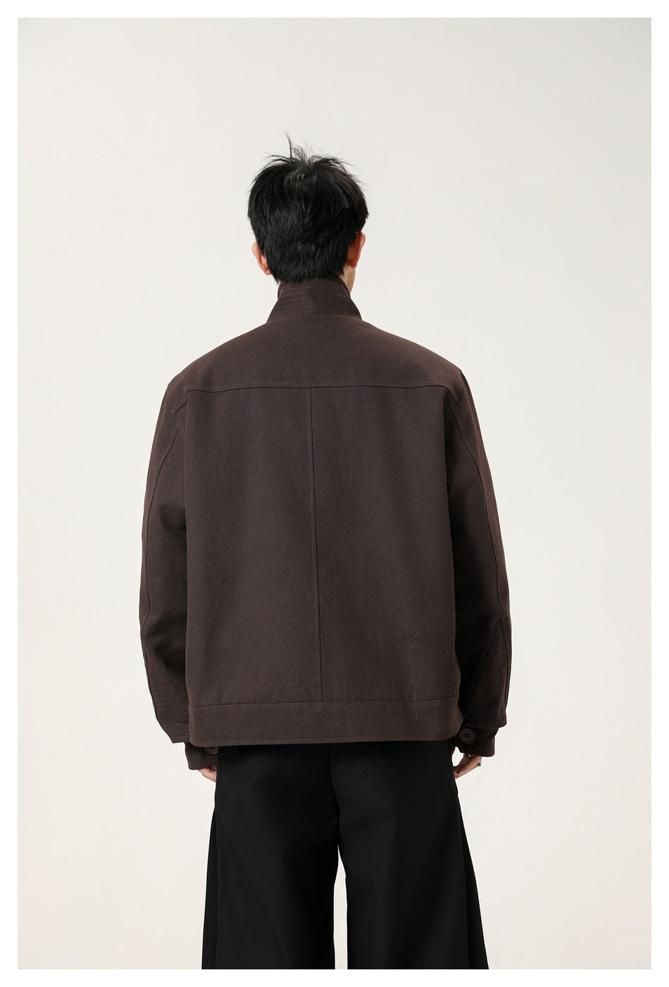 Back view of a man in a dark brown jacket showing the stand collar, back yoke seam, center seam and wide black trousers