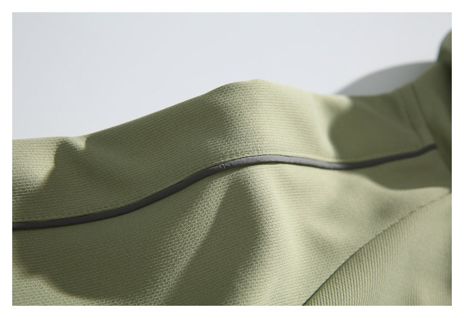 Close-up of curved dark piping across textured sage-green jacket fabric.