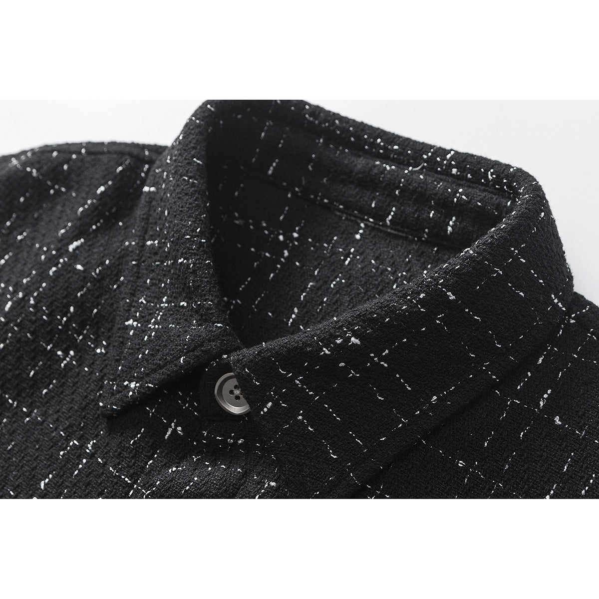 Close-up of the pointed collar and gray button on a black shirt with a scattered white fleck pattern.
