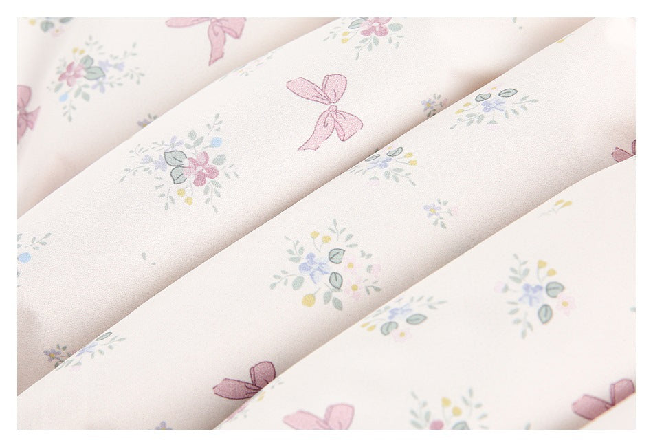 Macro view of pale ivory fabric with scattered pastel flowers and pink bow prints.