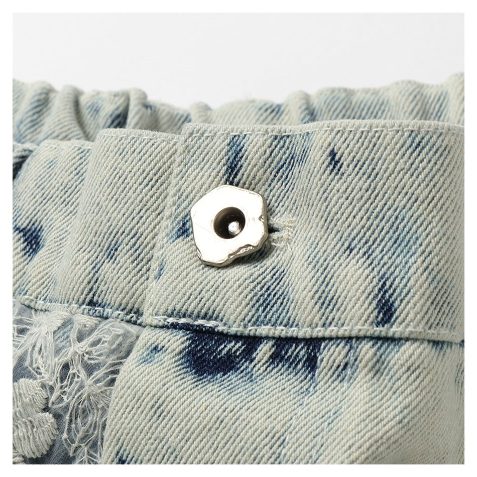 Close-up of a light-wash denim waistband with a metal button, dark blue markings, and a frayed embroidered edge.
