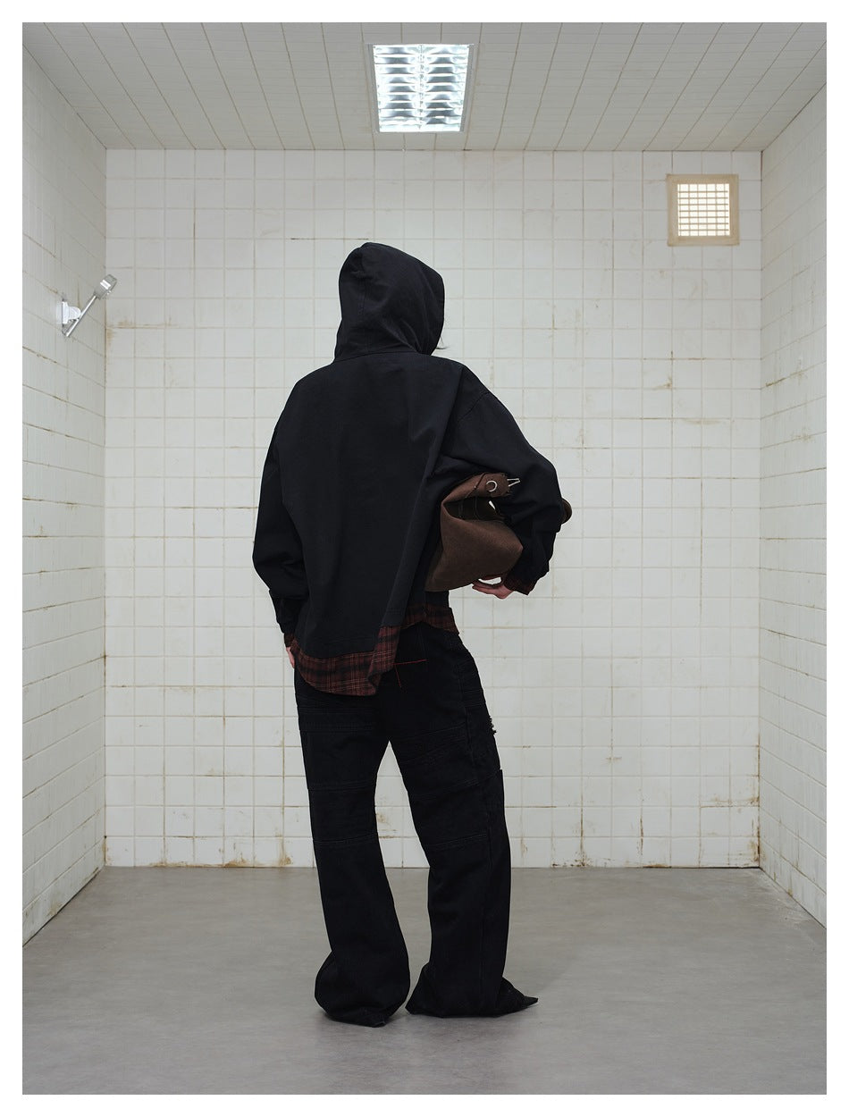 Back view of a model wearing a black hooded jacket with burgundy plaid trim and loose black pants.