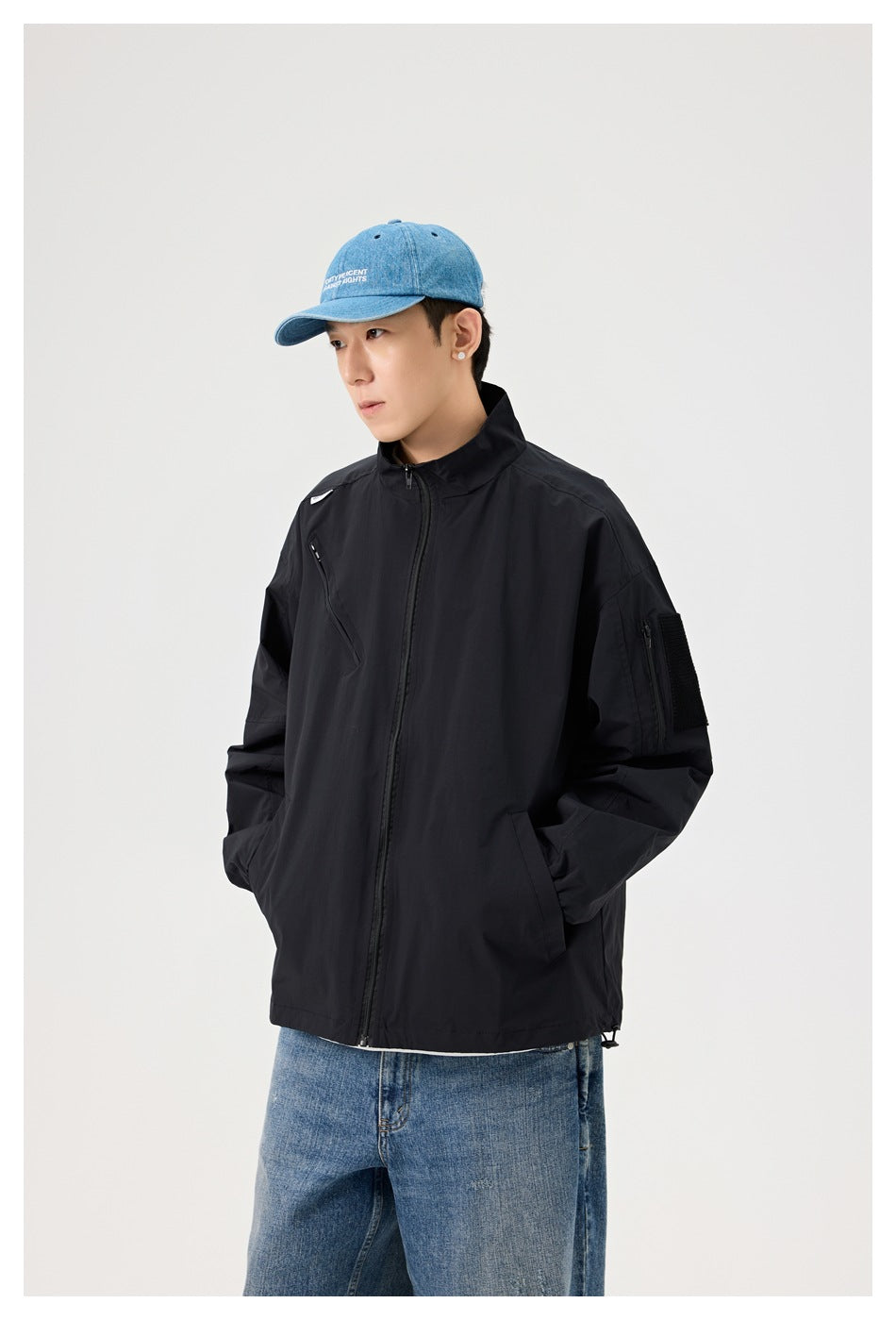 Model wearing a zipped black jacket with a stand collar, angled chest zip, and zippered sleeve pocket.