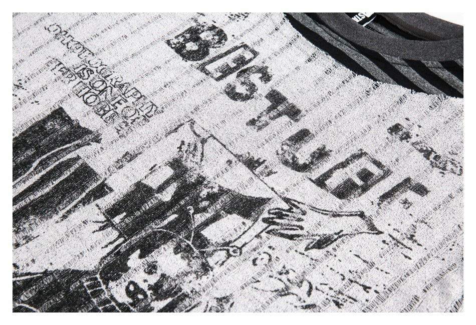 Angled close-up of black illustrated print and lettering on the light gray open-knit shirt.