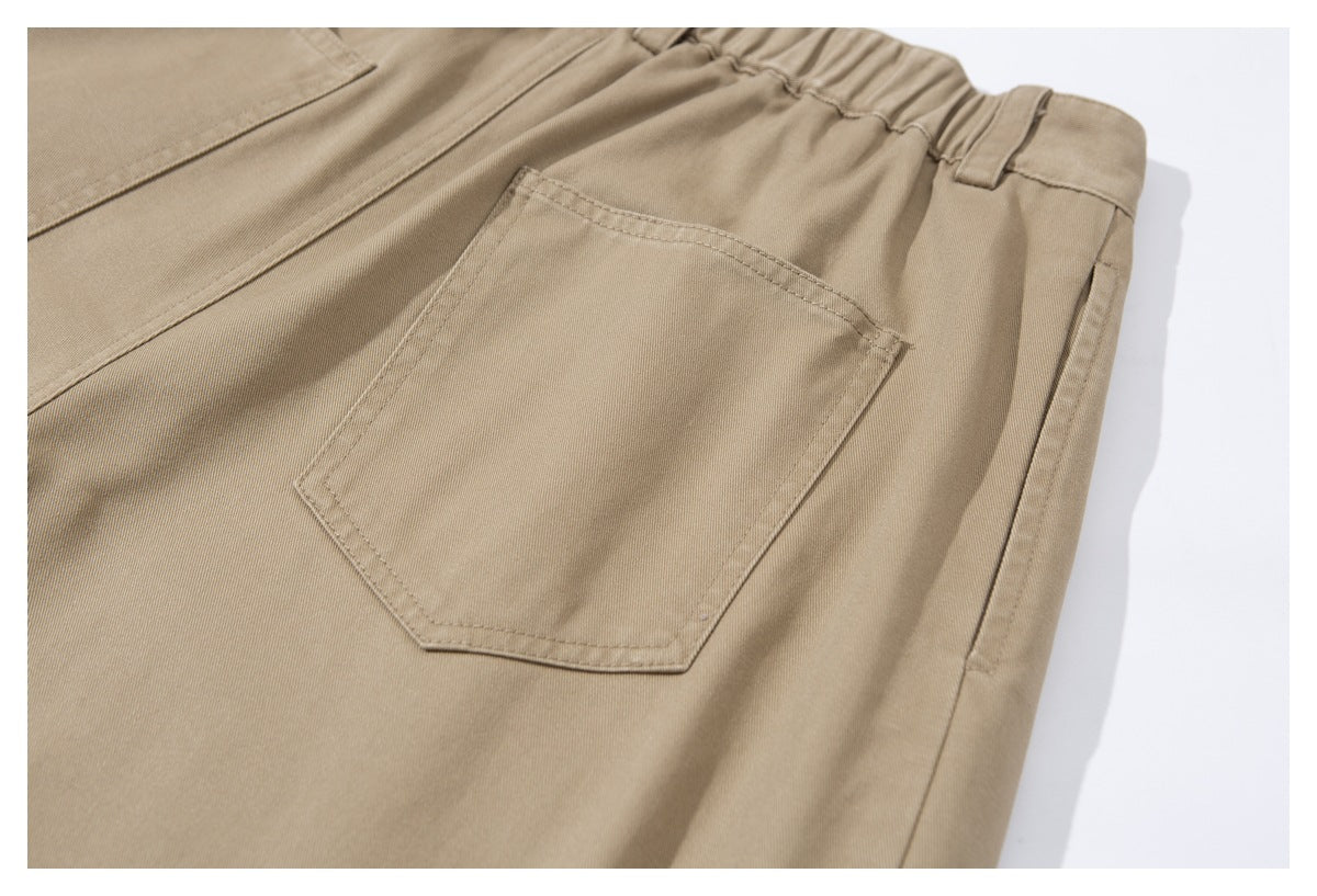 Close-up of tan trousers showing an elasticated waistband, belt loop and stitched rear patch pocket.