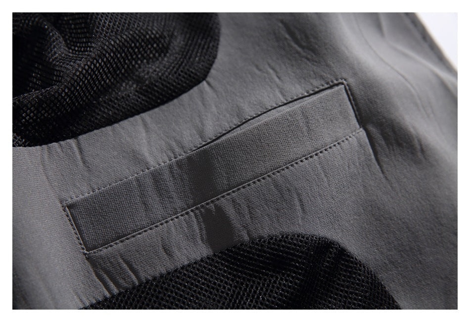 Close-up of a dark gray garment with a stitched pocket and black mesh panels.