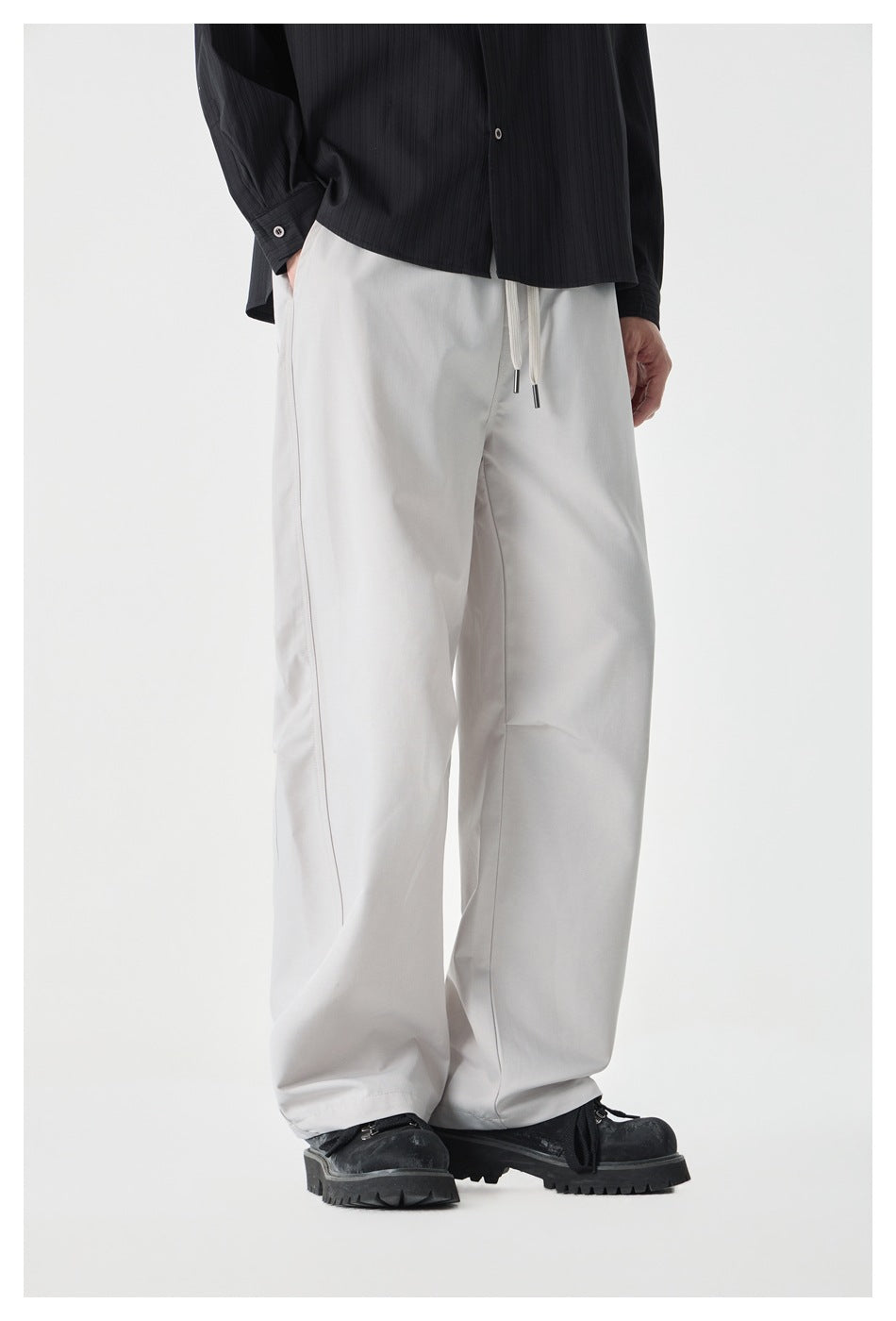 Model wearing beige wide-leg drawstring pants with a black striped shirt and chunky black shoes, side angle