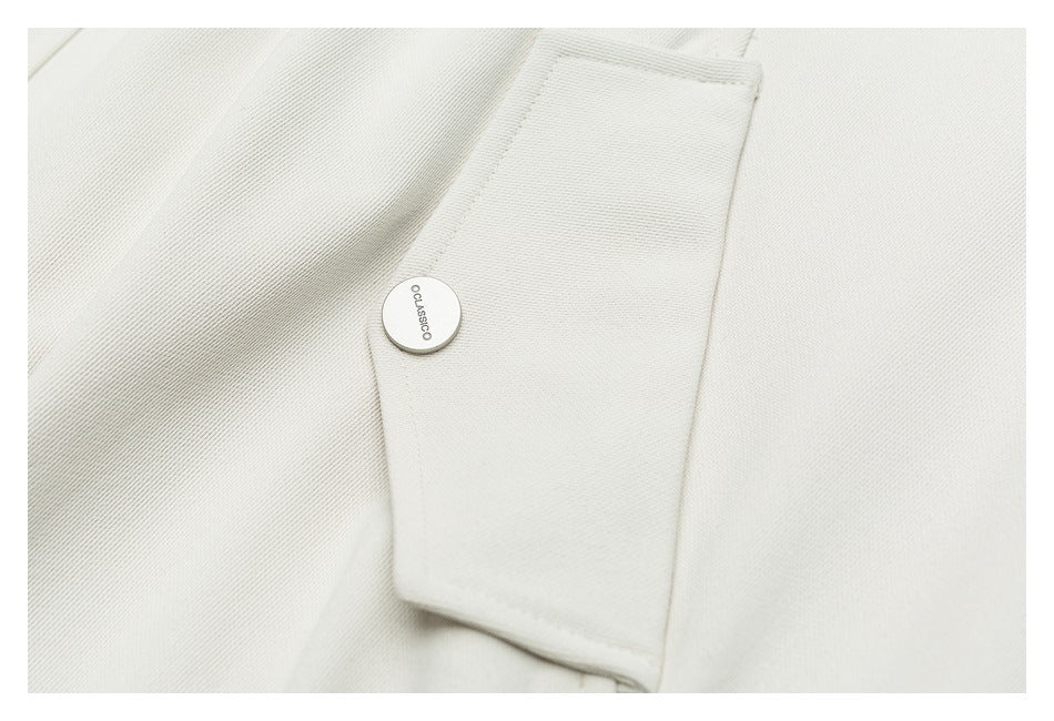 Close-up of an off-white garment tab with a small round button and stitched edges.