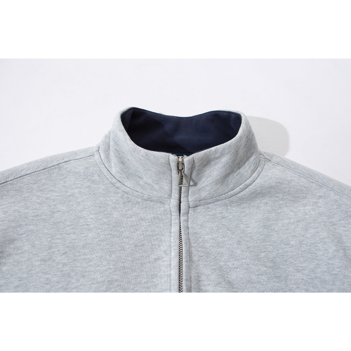 Close-up of a light gray zip-up jacket's raised collar, dark lining, and metal zipper.