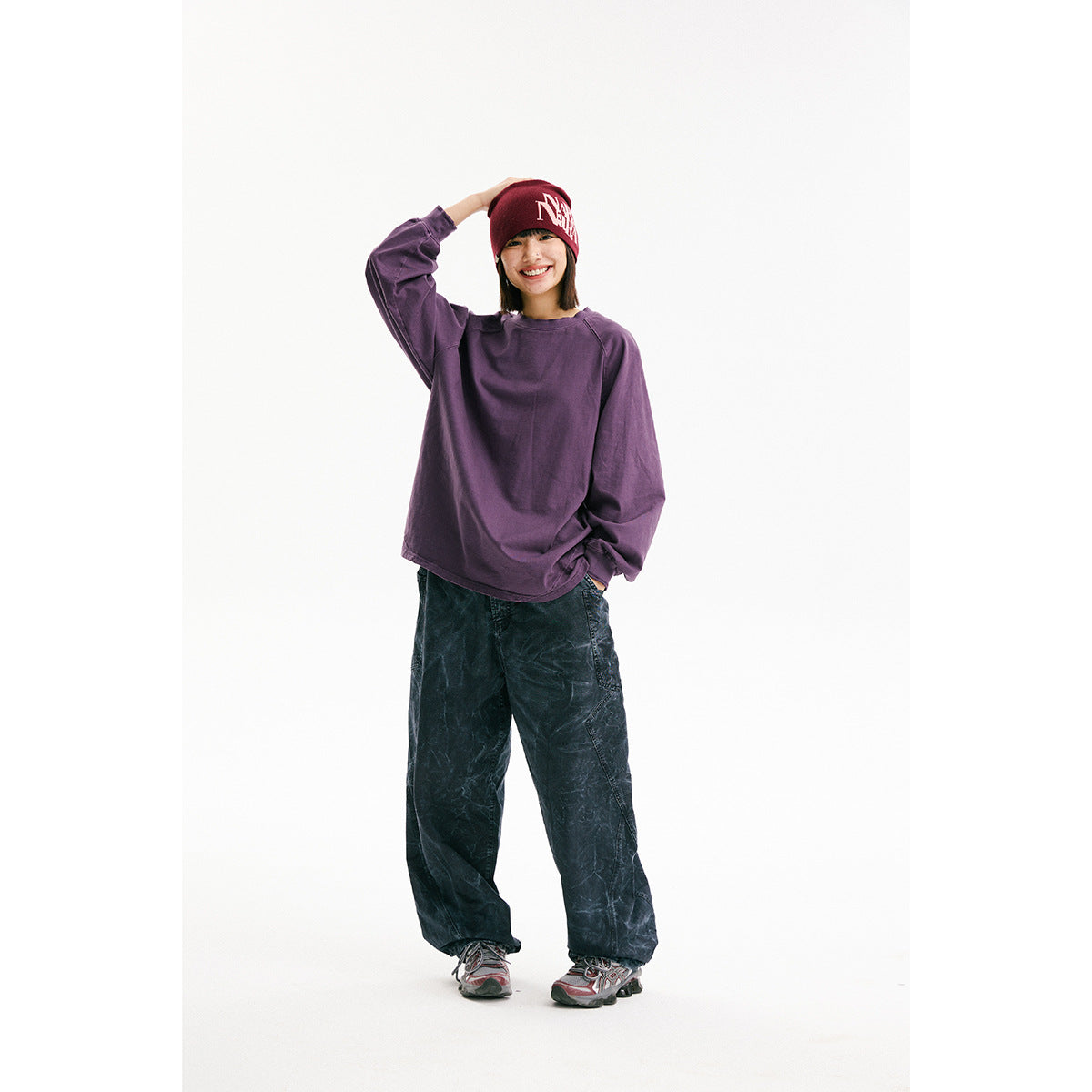 Model wearing an oversized purple long-sleeve shirt and dark loose pants, with a burgundy beanie.