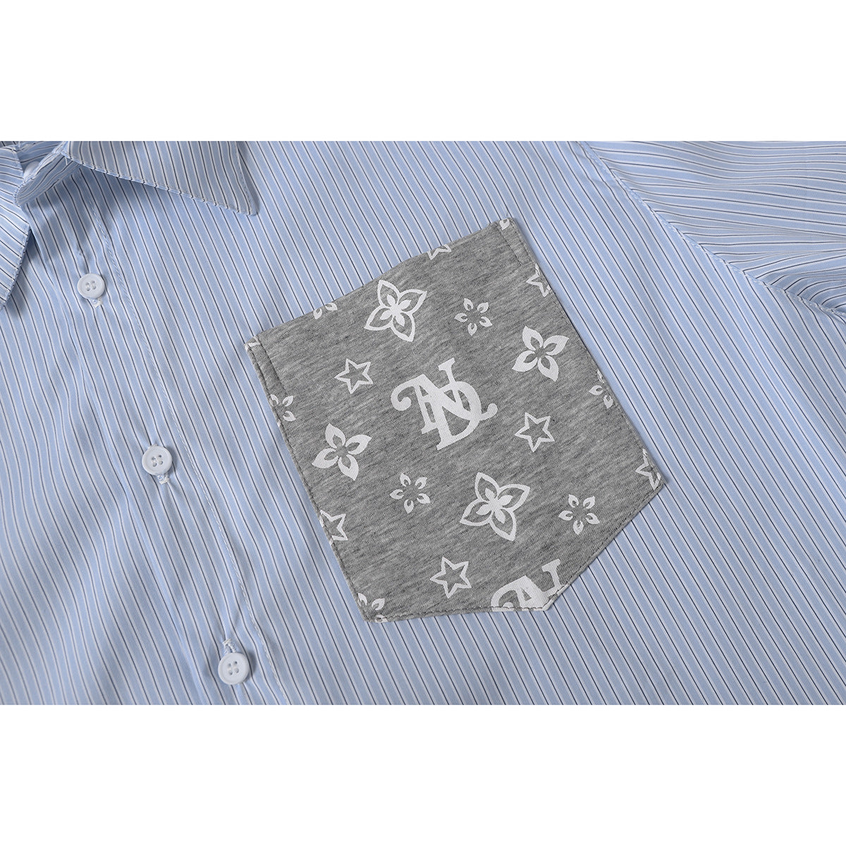Close-up of a light blue pinstriped shirt with white buttons and a gray pocket printed with flowers, stars, and a monogram.