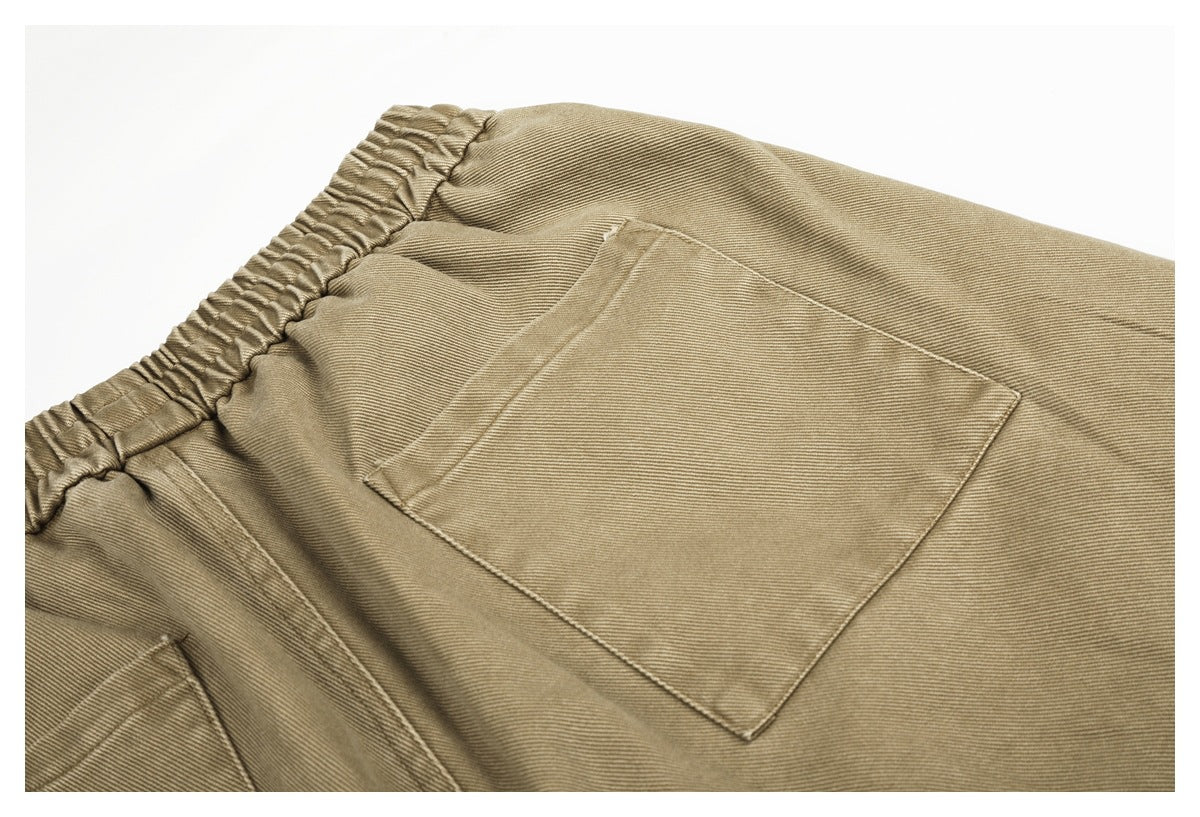 Close-up of tan trousers showing an elastic waistband and a large patch pocket.