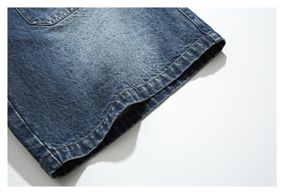 Close-up of the stitched leg opening and hem of dark blue washed denim trousers.