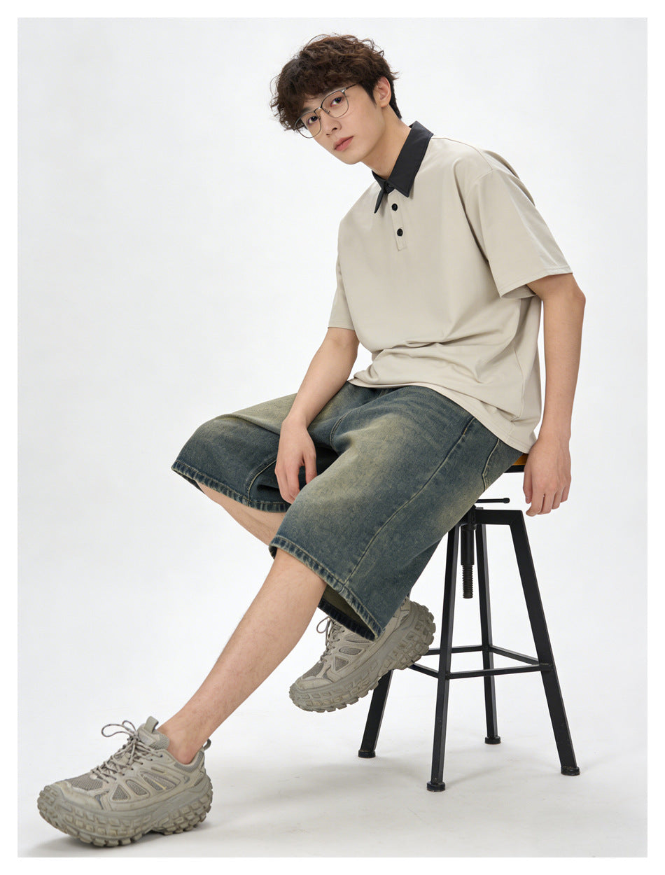 Model seated on a stool wearing a cream polo with black collar and buttons, faded denim shorts, and gray sneakers.