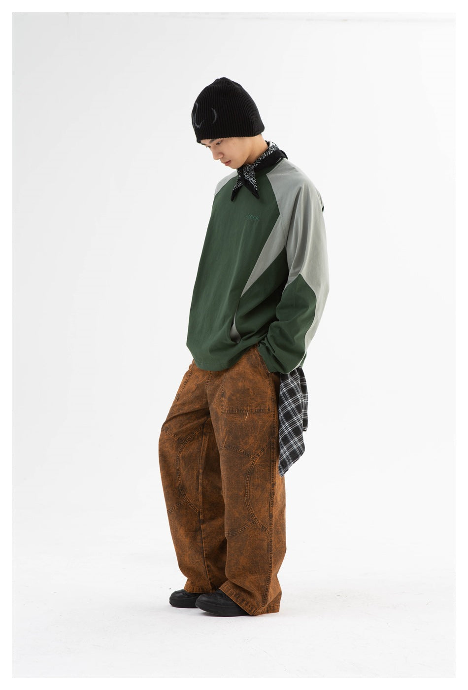 Three-quarter view of a model wearing a forest-green sweatshirt with pale gray raglan panels and loose brown pants.