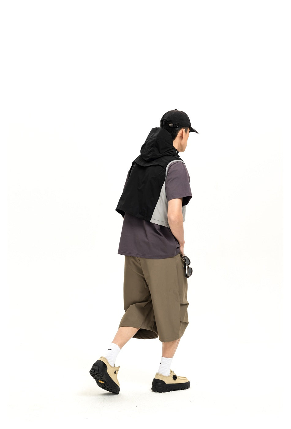 Rear three-quarter view of a model wearing a black hooded vest with pale side panels over a purple T-shirt.