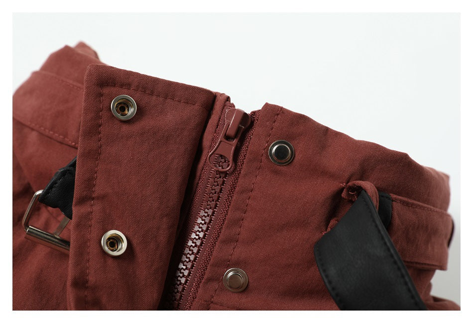 Close-up of the rust-red garment's front zipper, snap fasteners and black belt.