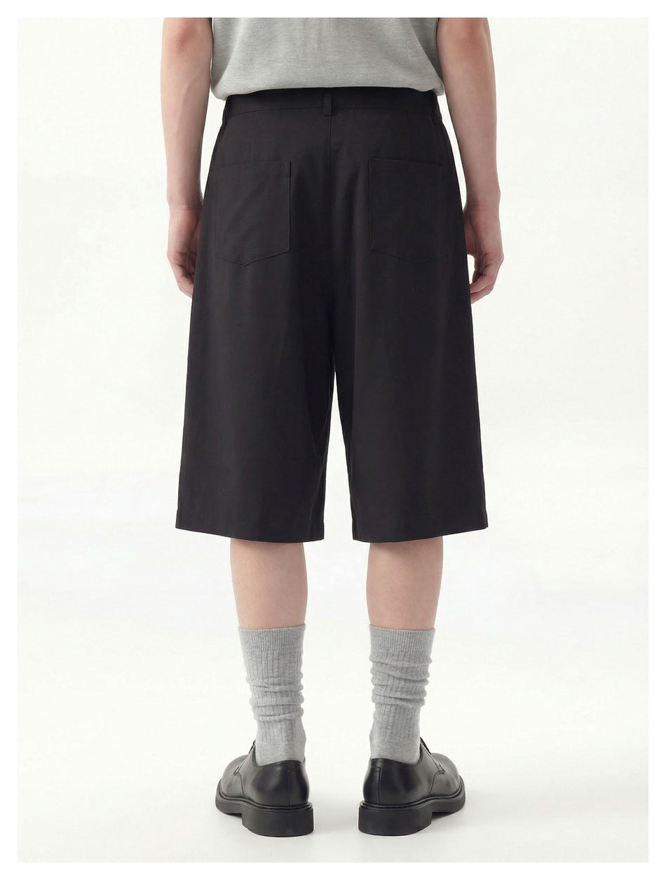 Rear view of a model wearing black knee-length shorts with two back patch pockets.