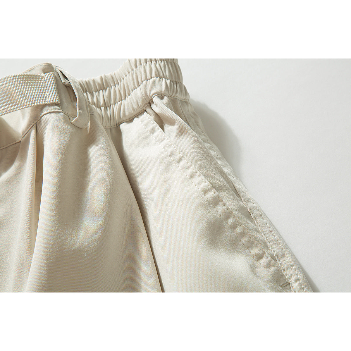 Close-up of cream shorts showing the elastic waistband, belt loop, and side pocket stitching.