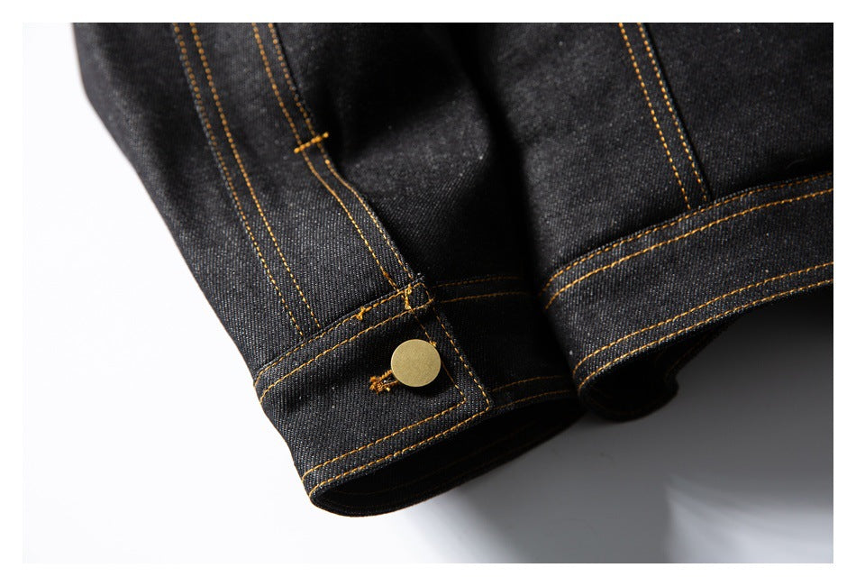 Close-up of black denim cuffs with brass-colored buttons and golden contrast stitching.