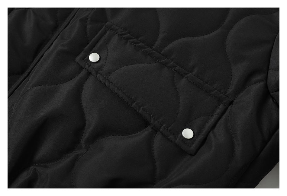Close-up of a black quilted jacket with curved stitching and two silver snap buttons.