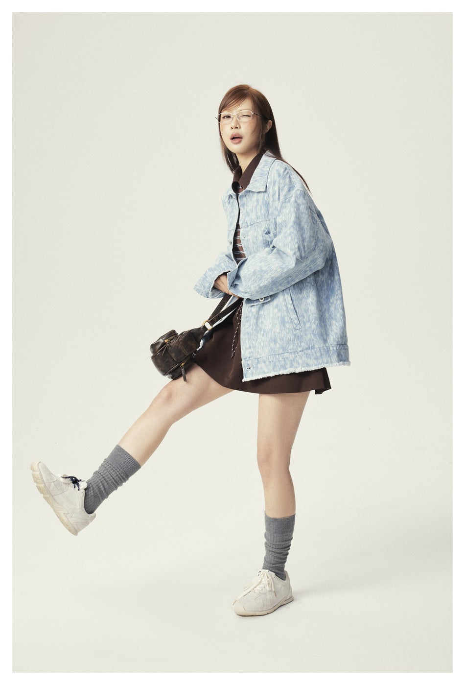 Model in a posed shot wearing an oversized light blue denim jacket with a brown skirt and a dark shoulder bag