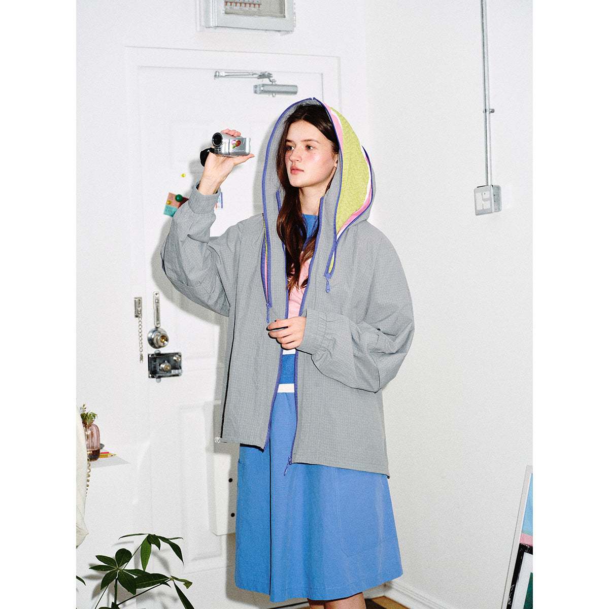 Model wears a gray hooded jacket with blue trim and bright yellow-pink lining over a blue dress.