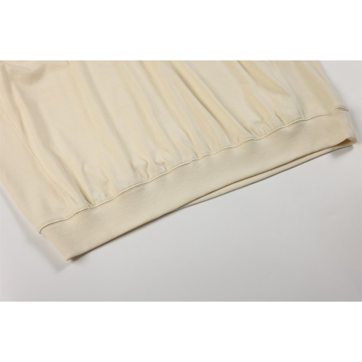 Close-up of the ivory sweatshirt's gathered lower edge and wide ribbed waistband.