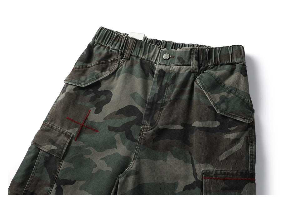 Cropped front view of dark green camouflage cargo shorts with an elastic waist, button and flap pockets.
